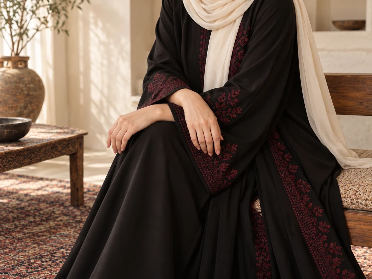 Cropped view of burgundy-embroidered black abaya sleeves and an ivory hijab